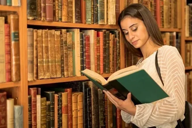 Young woman studying with an open book in a library. Student browsing books and reading in a traditional library.